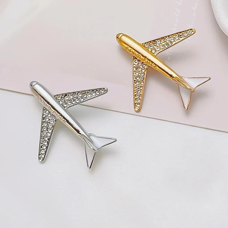 Gold and silver airplane shaped jewelry accessories displayed on light pink surface