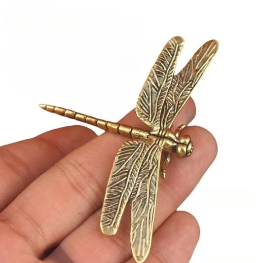 Gold dragonfly-shaped figurine held between fingers on a white background