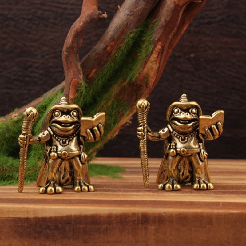 Two gold frog figurines with warrior poses on a wooden surface.