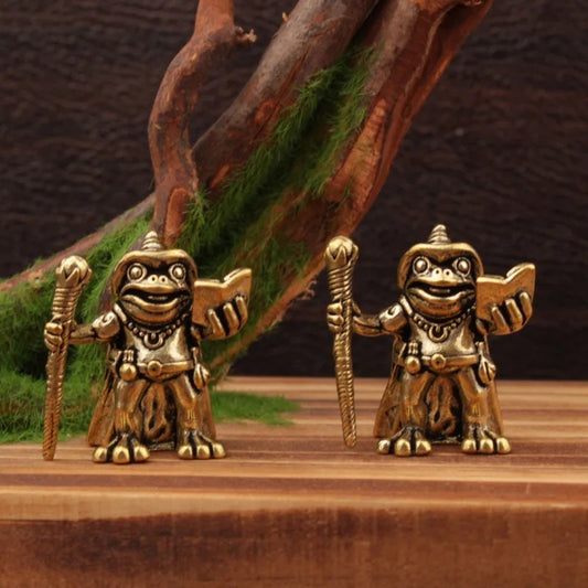 Two gold frog figurines with warrior poses on a wooden surface.