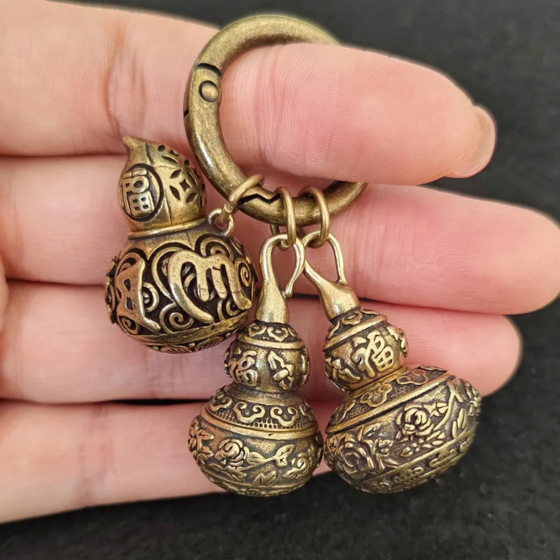 Bronze decorative keychain held between fingers against a dark background