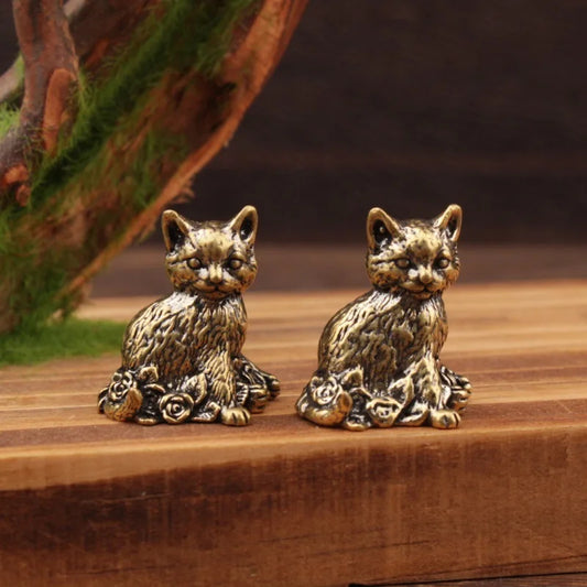 Two bronze cat figurines on a wooden surface with a natural background.