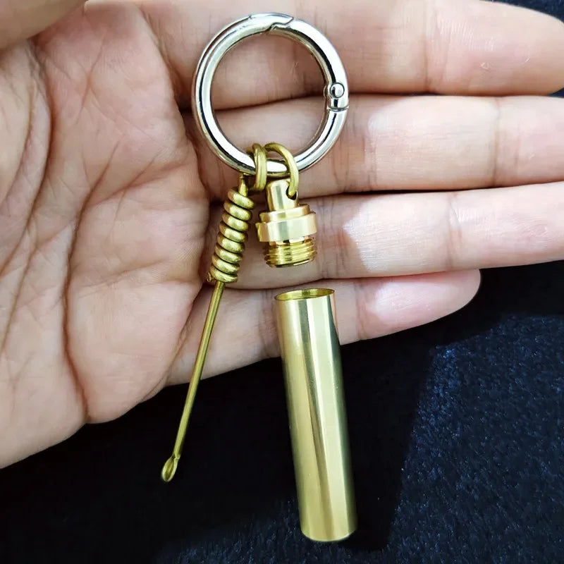 Brass alloy keychain with portable storage tube and mini tool accessory on black background