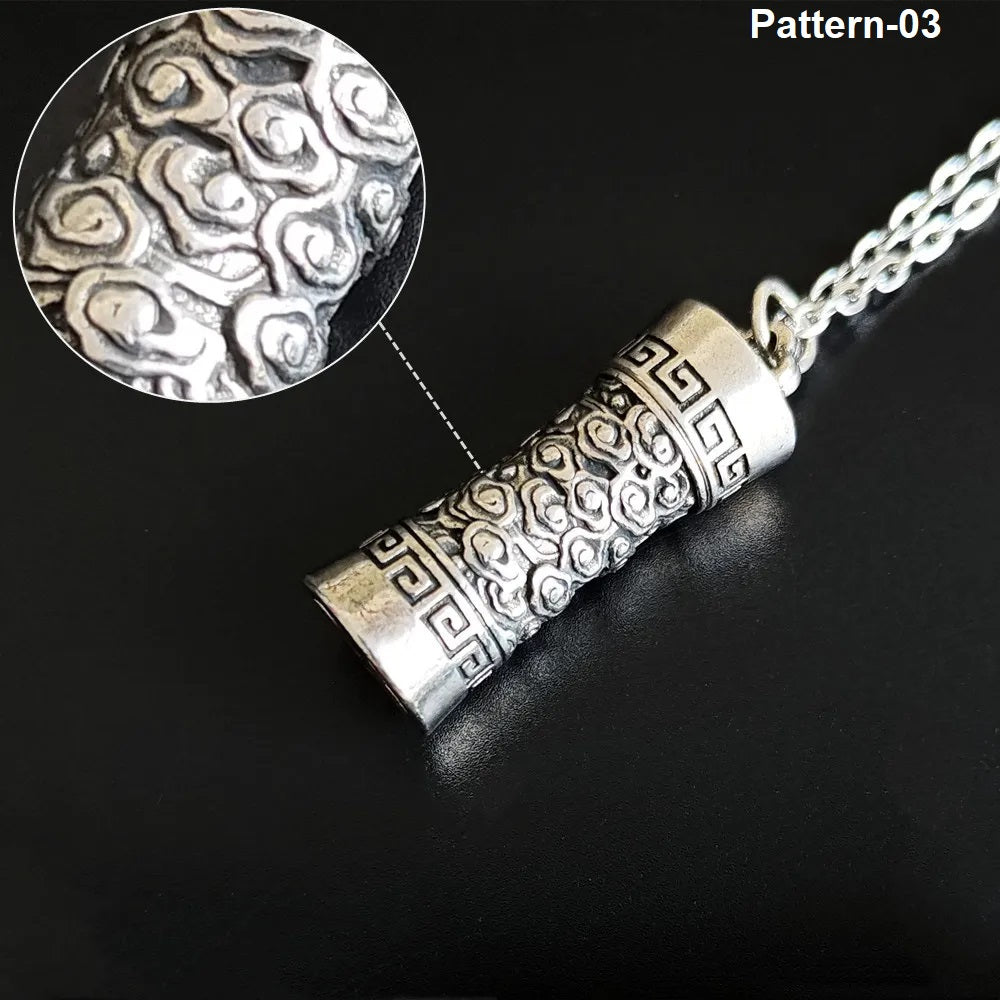 Silver cylindrical pendant with intricate patterns on a black background