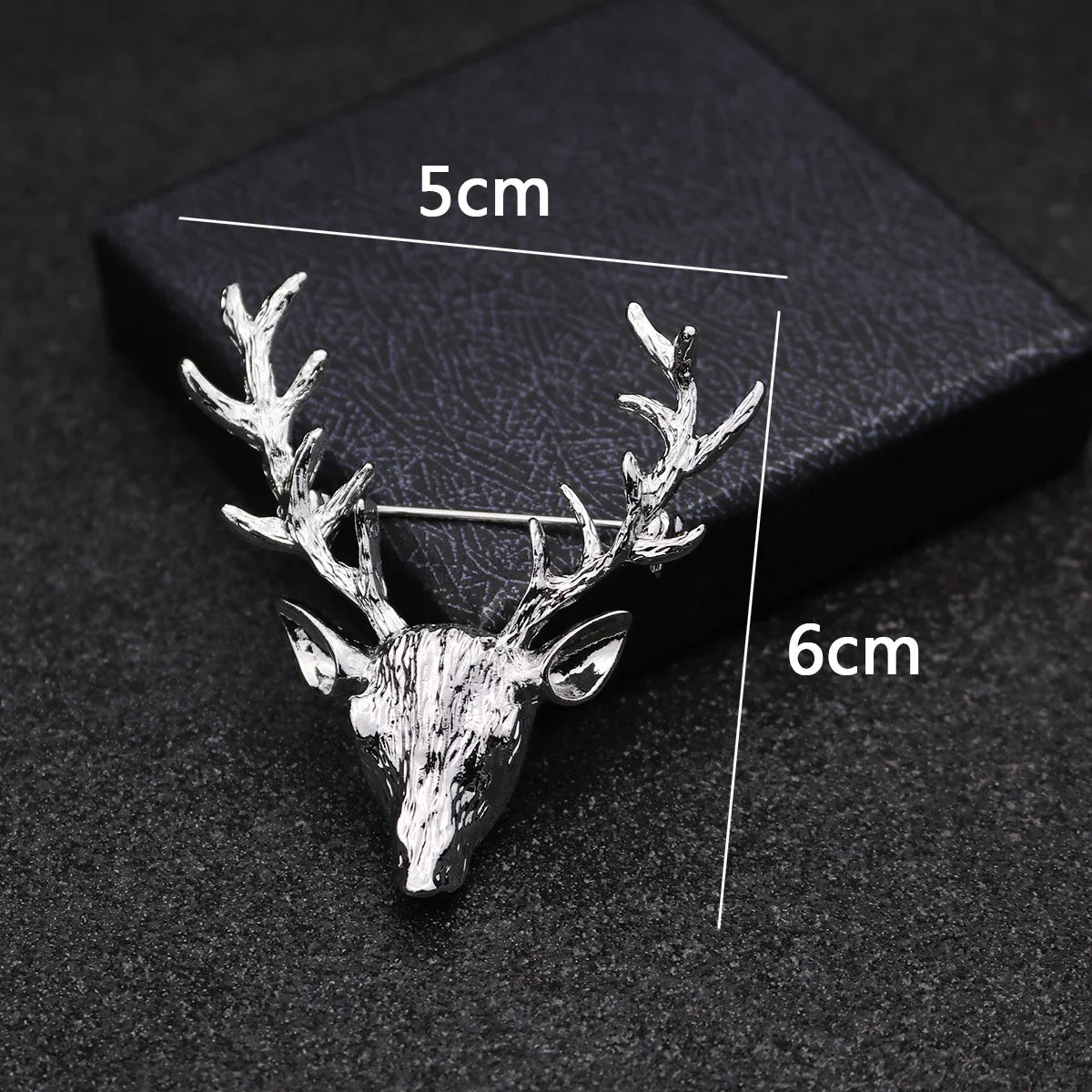Silver deer head brooch with measurements on a dark background