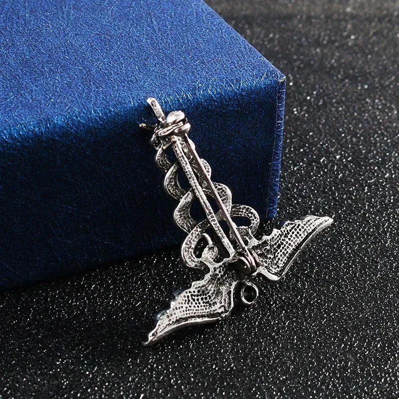 Silver caduceus brooch on a black surface with a blue box in the background