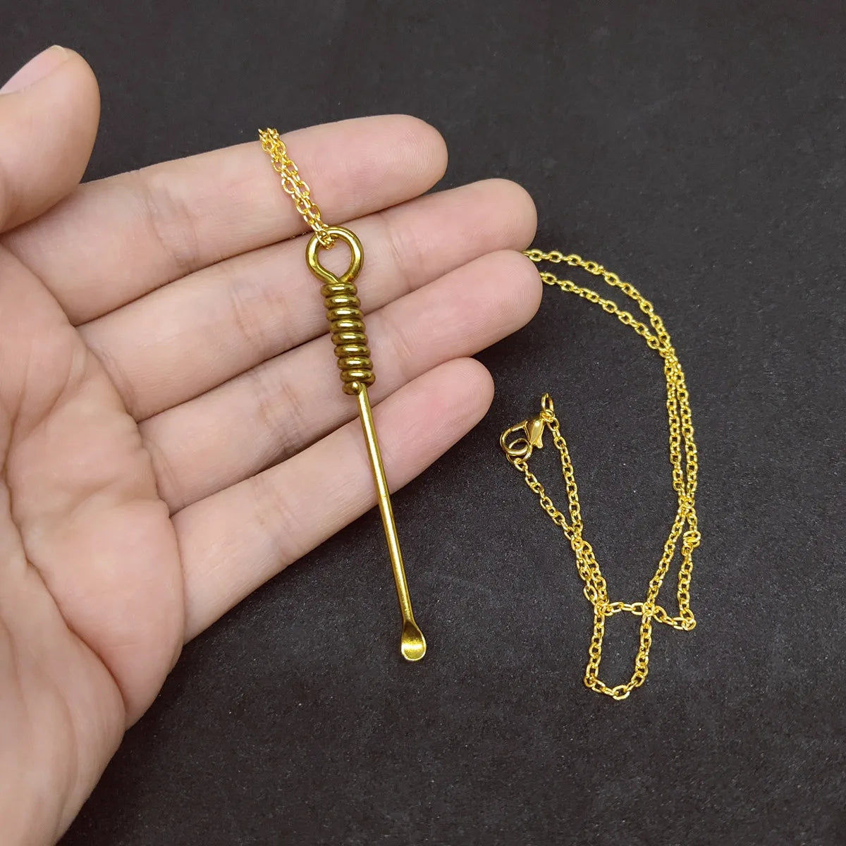 Handheld gold spoon charm necklace showcasing detailed metal design and craftsmanship