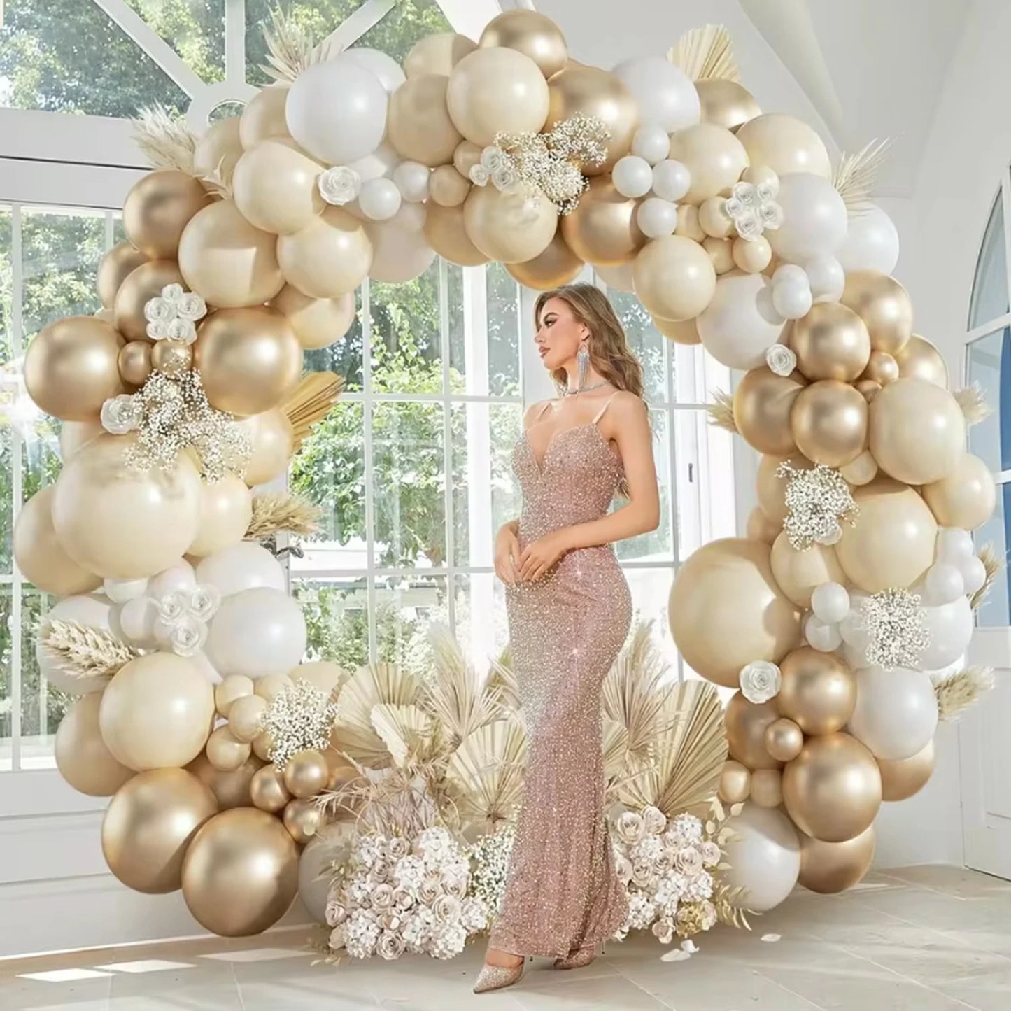 Woman in a pink dress standing in front of a large balloon arch with gold and white balloons.